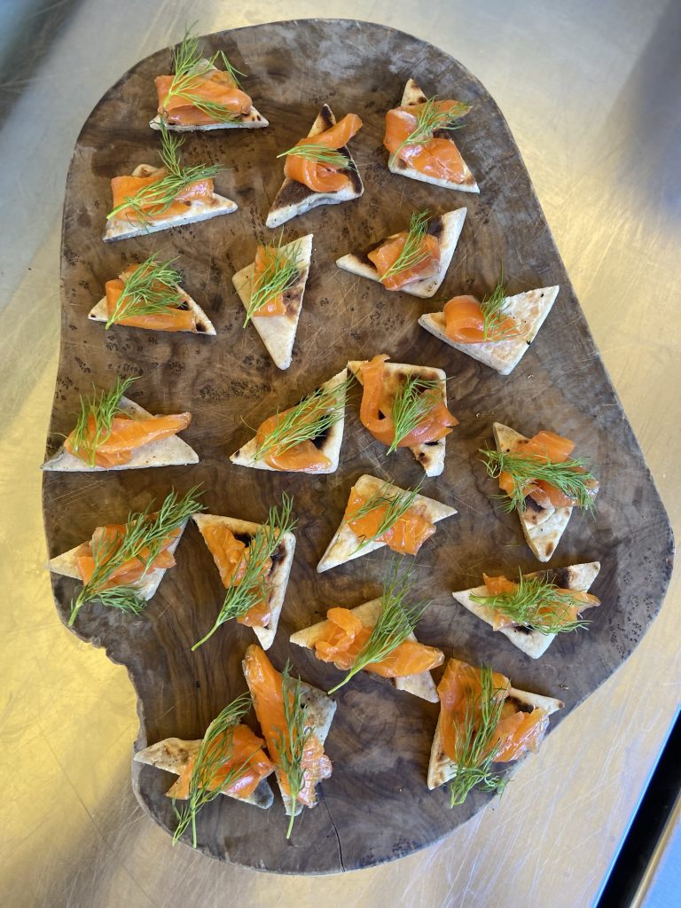 A wooden tray with several trout canapés 